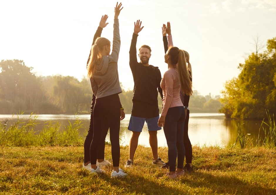 A group of people raises their hands together by a lakeside at sunset - Jersey Integrative Health and Wellness A group of people raises their hands together by a lakeside at sunset - Jersey Integrative Health and Wellness